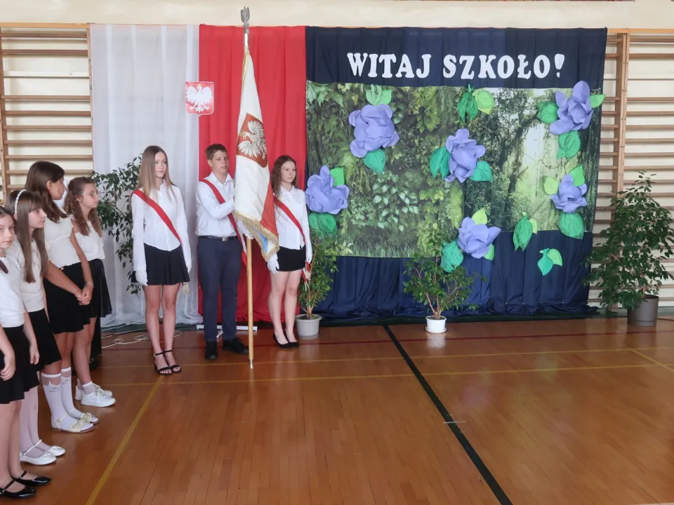 Poczet sztandarowy i uczniowie przed szkolną dekoracją.