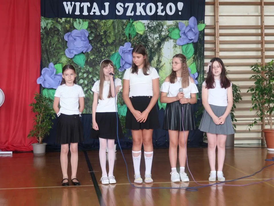 Grupa uczniów występująca przed szkolną dekoracją.
