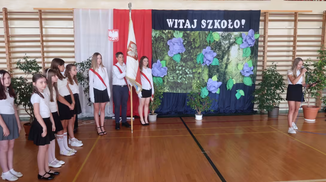 Poczet sztandarowy i uczniowie przed szkolną dekoracją.